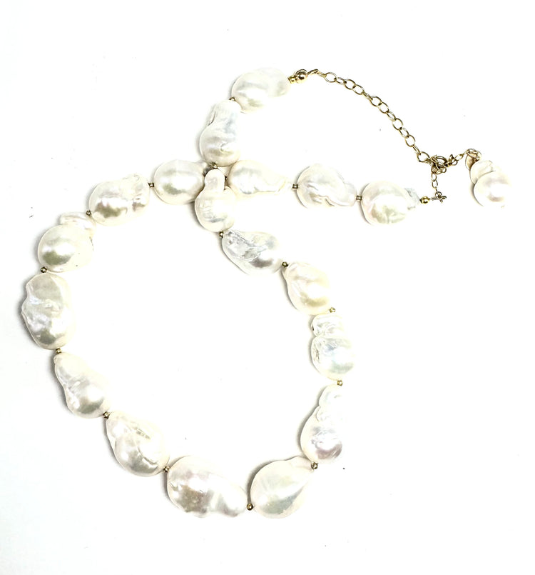 Collier sur chaîne en or laminé - Perles keshi (perles de culture dites "baroques") 1,5cm environ, perles en or laminé 14 carats.
Ce collier met à l’honneur la perle keshi dans toute son authenticité. Chaque perle, naturellement formée, révèle des reflets nacrés et une texture organique qui en font une pièce unique. Assemblées à la main, elles composent un bijou à la fois moderne, raffiné et intemporel