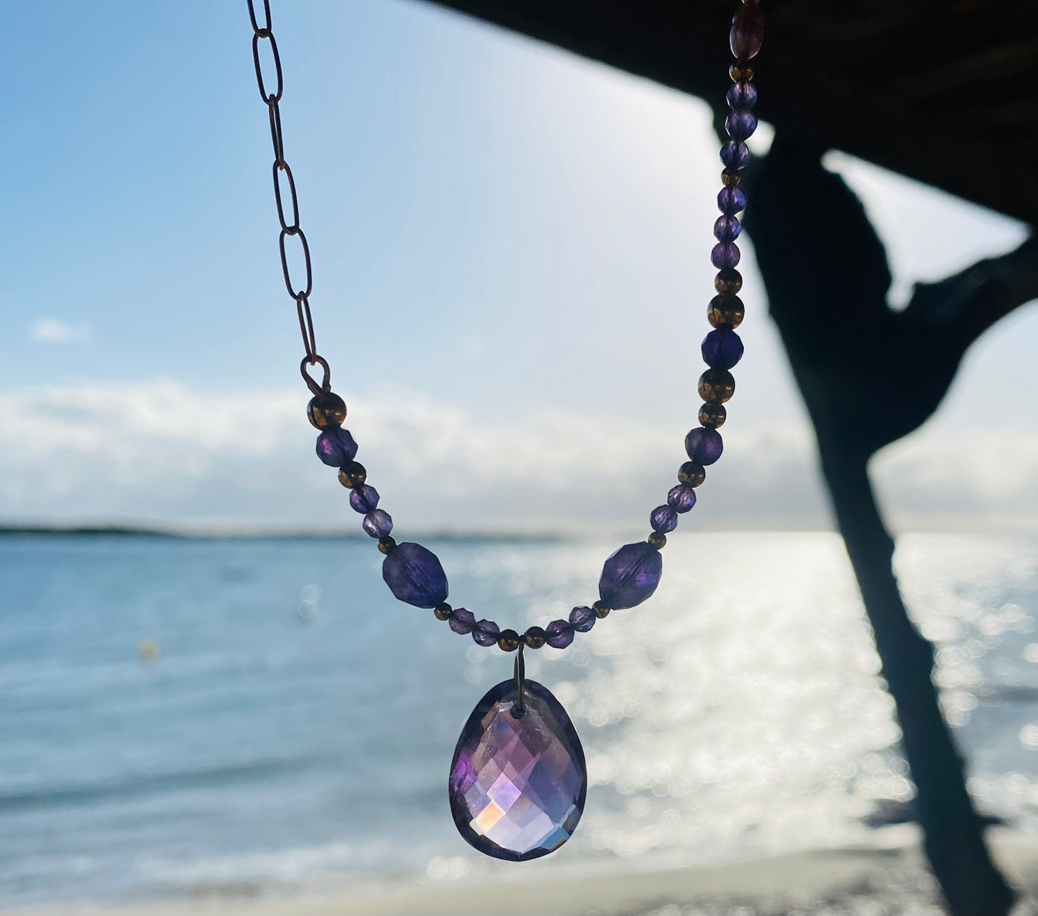 Collier améthyste fait main, pierre naturelle, bijou Corse, chaîne bronze, pendentif facetté, plage en arrière-plan