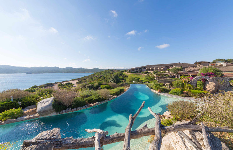 Paysage côtier corse avec piscine infinie, vue sur la mer et végétation méditerranéenne sous ciel bleu